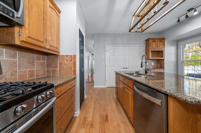 kitchen with decorative backsplash, appliances with stainless steel finishes, sink, light hardwood / wood-style flooring, and dark stone countertops