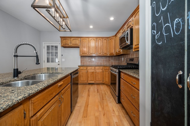 kitchen featuring decorative backsplash, appliances with stainless steel finishes, light wood-type flooring, sink, and dark stone countertops