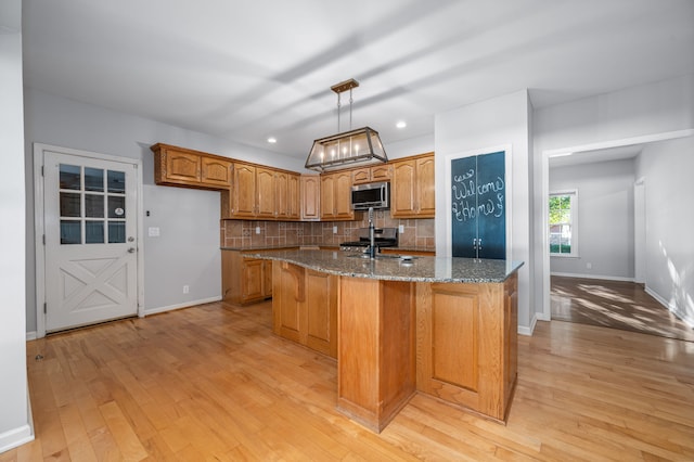 kitchen with appliances with stainless steel finishes, decorative light fixtures, dark stone countertops, light hardwood / wood-style floors, and an island with sink