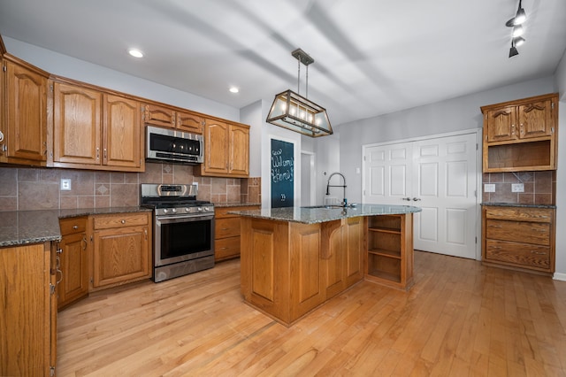 kitchen featuring sink, backsplash, an island with sink, appliances with stainless steel finishes, and light wood-type flooring