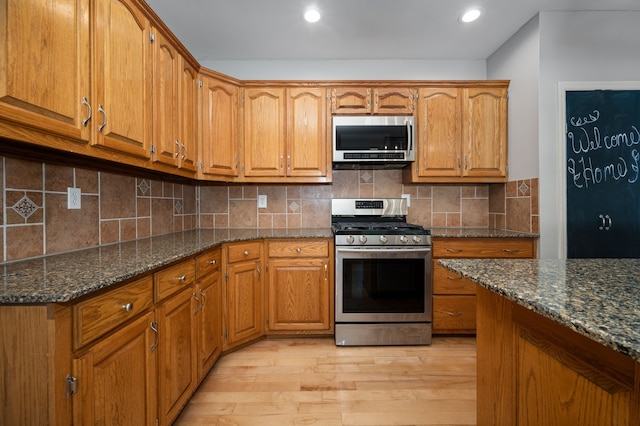 kitchen featuring tasteful backsplash, light wood-type flooring, appliances with stainless steel finishes, and dark stone counters