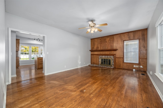 unfurnished living room with a fireplace, hardwood / wood-style flooring, ceiling fan, and wood walls