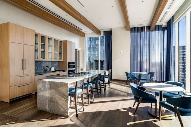 kitchen featuring light brown cabinetry, backsplash, dark wood-type flooring, beamed ceiling, and a kitchen island