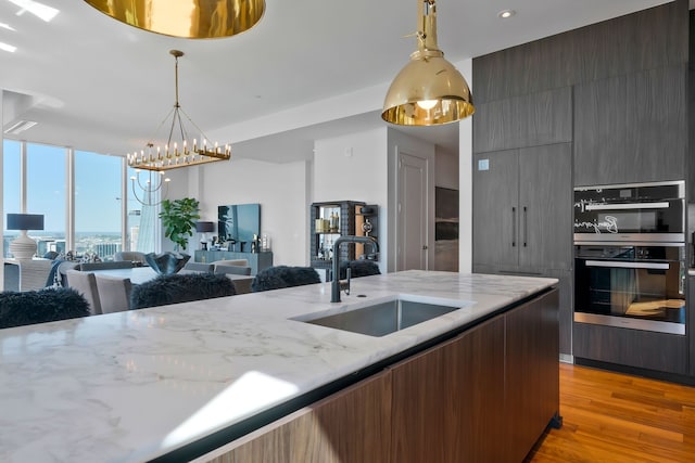 kitchen with light stone countertops, sink, double oven, light hardwood / wood-style floors, and decorative light fixtures