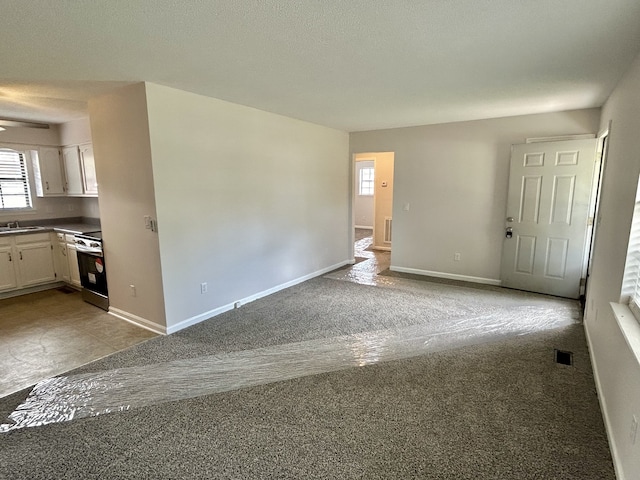 unfurnished living room with a textured ceiling, light colored carpet, and sink