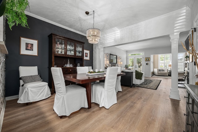 dining room featuring decorative columns, crown molding, light hardwood / wood-style flooring, and french doors