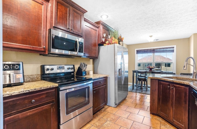 kitchen featuring light stone countertops, sink, a textured ceiling, and appliances with stainless steel finishes