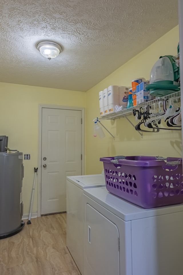 washroom with light wood-type flooring, a textured ceiling, electric water heater, and washing machine and clothes dryer