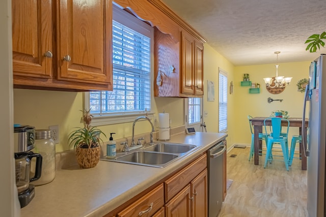 kitchen with sink, a notable chandelier, pendant lighting, a textured ceiling, and appliances with stainless steel finishes