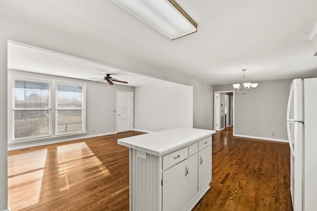 kitchen with dark hardwood / wood-style flooring, ceiling fan with notable chandelier, a kitchen island, white fridge, and white cabinetry