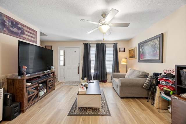 living room featuring ceiling fan, light hardwood / wood-style flooring, and a textured ceiling