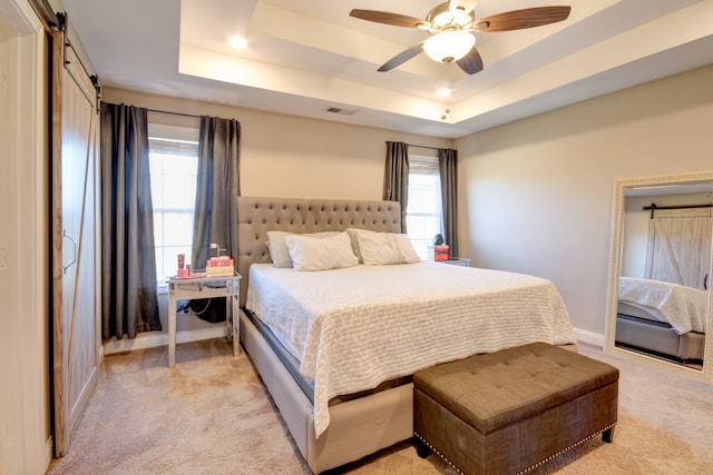 bedroom with a tray ceiling, a barn door, ceiling fan, and light colored carpet