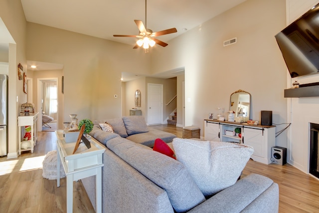 living room with ceiling fan, light wood-type flooring, and a high ceiling