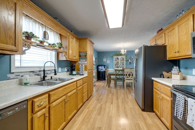 kitchen with sink, light hardwood / wood-style flooring, appliances with stainless steel finishes, hanging light fixtures, and a textured ceiling