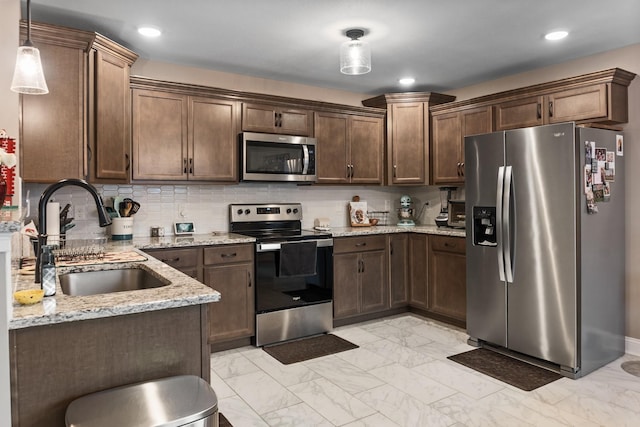 kitchen with sink, stainless steel appliances, light stone countertops, decorative backsplash, and decorative light fixtures