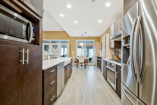 kitchen featuring decorative backsplash, stainless steel appliances, an inviting chandelier, light hardwood / wood-style flooring, and hanging light fixtures