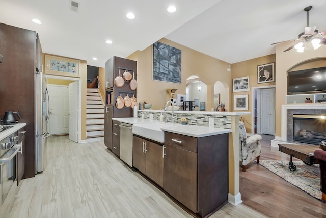 kitchen featuring dark brown cabinetry, sink, stainless steel appliances, a tiled fireplace, and decorative backsplash