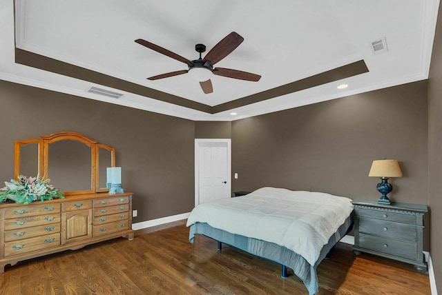 bedroom featuring dark hardwood / wood-style floors, ceiling fan, ornamental molding, and a tray ceiling