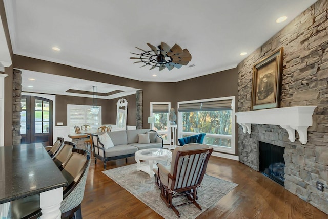 living room with dark hardwood / wood-style floors, a stone fireplace, and crown molding