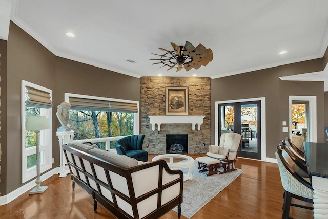 living room with wood-type flooring, a stone fireplace, ceiling fan, and crown molding