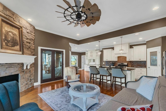 living room with ornamental molding, ceiling fan, dark wood-type flooring, sink, and a stone fireplace