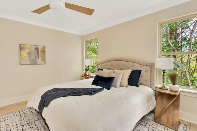 bedroom featuring ceiling fan, crown molding, light hardwood / wood-style flooring, and multiple windows