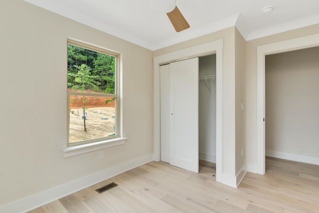 unfurnished bedroom with ceiling fan, a closet, crown molding, and light wood-type flooring