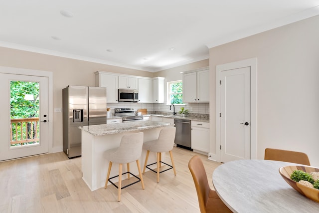 kitchen featuring a center island, decorative backsplash, light wood-type flooring, white cabinetry, and stainless steel appliances