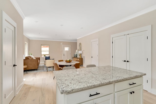 kitchen with light stone counters, white cabinetry, crown molding, and light hardwood / wood-style flooring