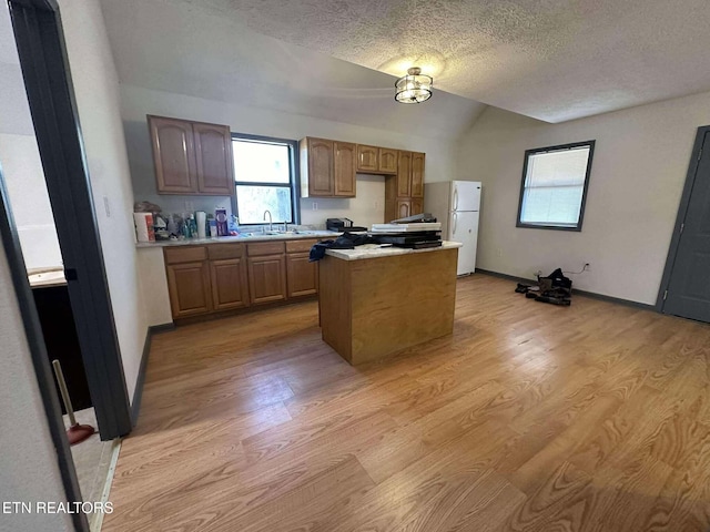 kitchen with white fridge, a center island, vaulted ceiling, and light hardwood / wood-style flooring