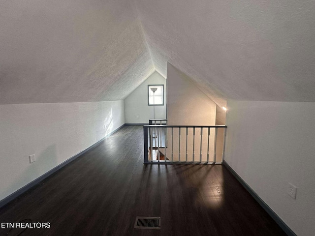 additional living space featuring a textured ceiling, dark wood-type flooring, and lofted ceiling