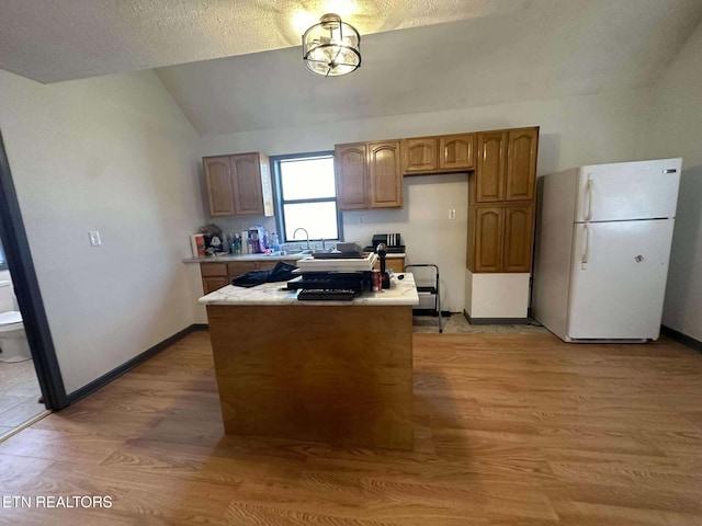 kitchen with a textured ceiling, light hardwood / wood-style floors, vaulted ceiling, and white refrigerator