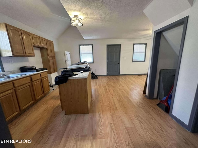 kitchen featuring a textured ceiling, light hardwood / wood-style flooring, a center island, white fridge, and lofted ceiling