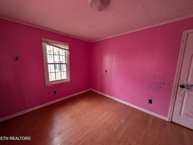 spare room featuring wood walls, wood-type flooring, and ornamental molding