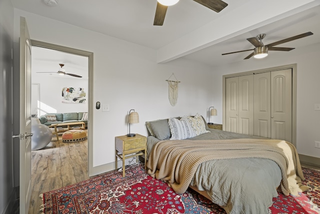 bedroom with beamed ceiling, wood-type flooring, a closet, and ceiling fan