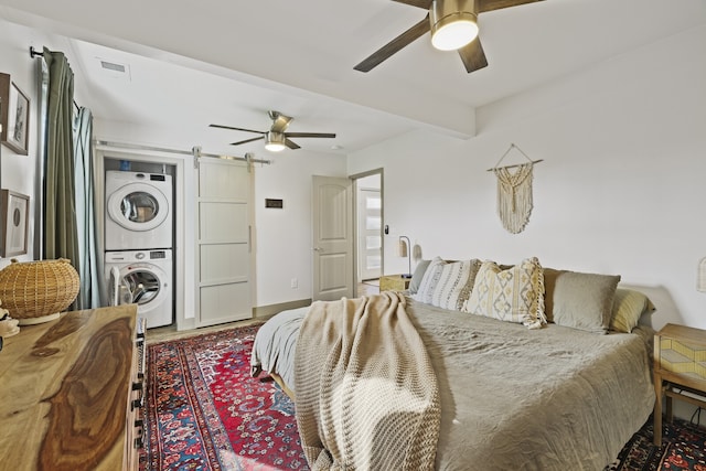 bedroom with beamed ceiling, a barn door, stacked washer / dryer, and ceiling fan