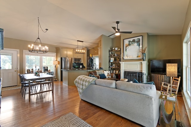 living room featuring sink, ceiling fan with notable chandelier, lofted ceiling, and light wood-type flooring