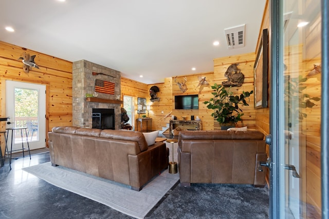 living room with ceiling fan, wood walls, and a stone fireplace