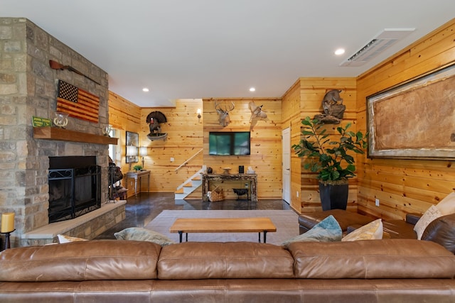 living room featuring a stone fireplace, wood walls, and concrete flooring