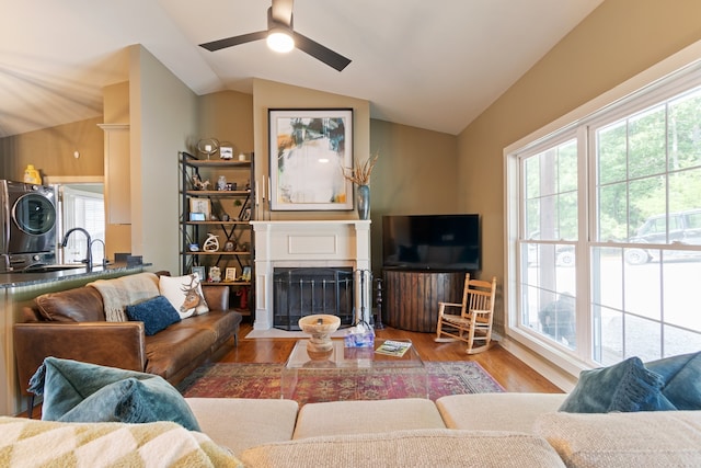 living room featuring sink, vaulted ceiling, hardwood / wood-style flooring, ceiling fan, and stacked washer / dryer