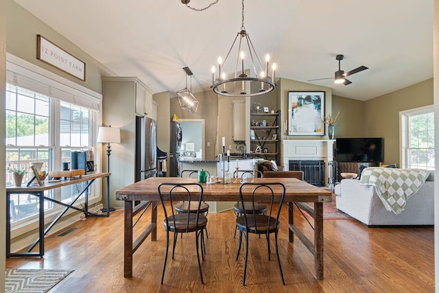 dining room featuring ceiling fan with notable chandelier, light hardwood / wood-style flooring, and vaulted ceiling