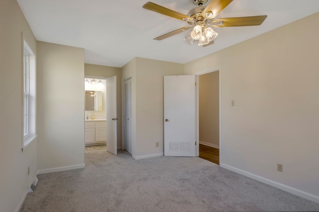 unfurnished bedroom with ensuite bath, ceiling fan, a closet, and light carpet