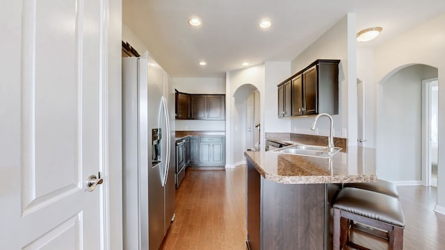 kitchen featuring a kitchen breakfast bar, sink, appliances with stainless steel finishes, dark brown cabinets, and wood-type flooring