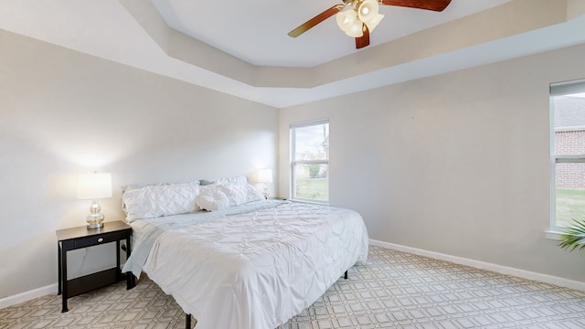 carpeted bedroom with a tray ceiling, multiple windows, and ceiling fan