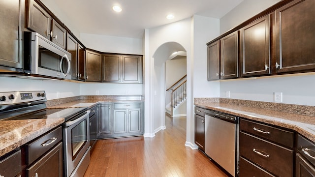 kitchen featuring light stone countertops, dark brown cabinets, light wood-type flooring, and appliances with stainless steel finishes