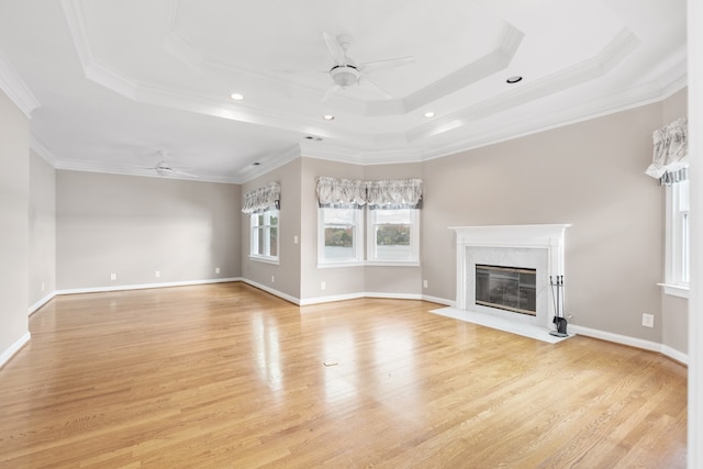 unfurnished living room featuring ornamental molding, a raised ceiling, ceiling fan, light hardwood / wood-style flooring, and a premium fireplace