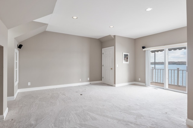 spare room featuring light carpet, a water view, and vaulted ceiling