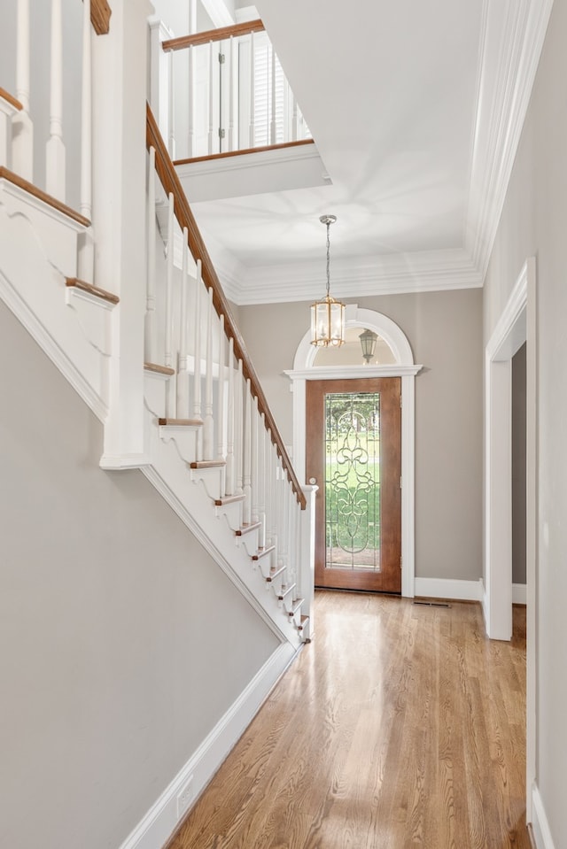 foyer entrance with an inviting chandelier, light hardwood / wood-style flooring, and crown molding