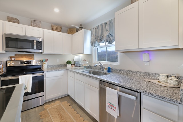 kitchen with appliances with stainless steel finishes, light stone counters, sink, light hardwood / wood-style floors, and white cabinetry