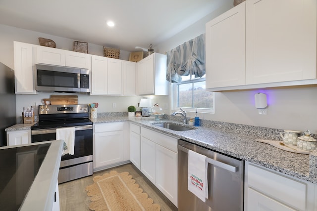 kitchen with light stone countertops, white cabinetry, sink, stainless steel appliances, and light hardwood / wood-style floors